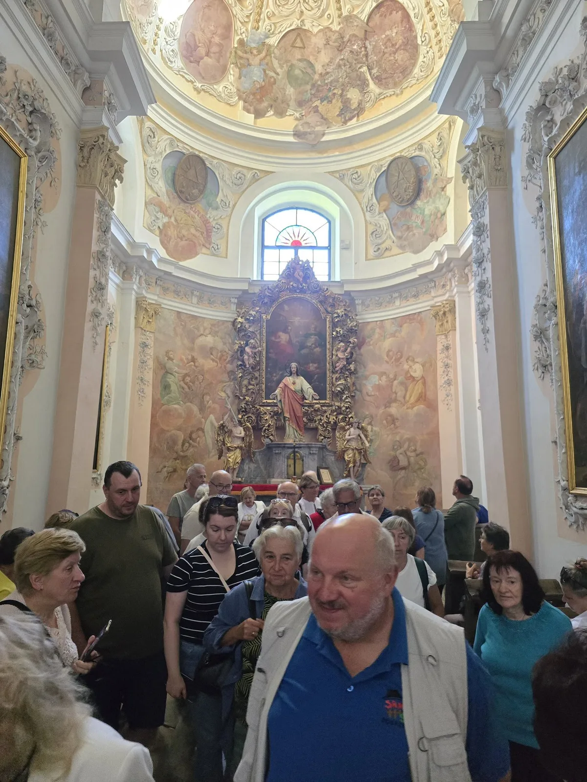 Uczestnicy wycieczki zwiedzają wnętrze z ołtarzem i malowidłami na sklepieniu.
