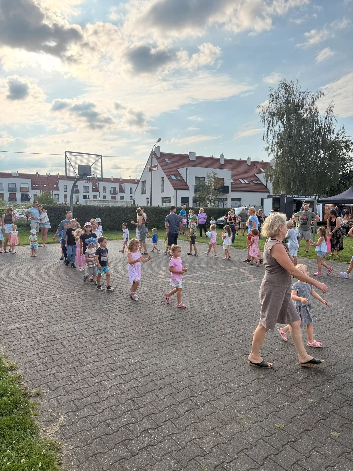 Dzieci i dorośli wspólnie tańczą na placu podczas letniego spotkania.