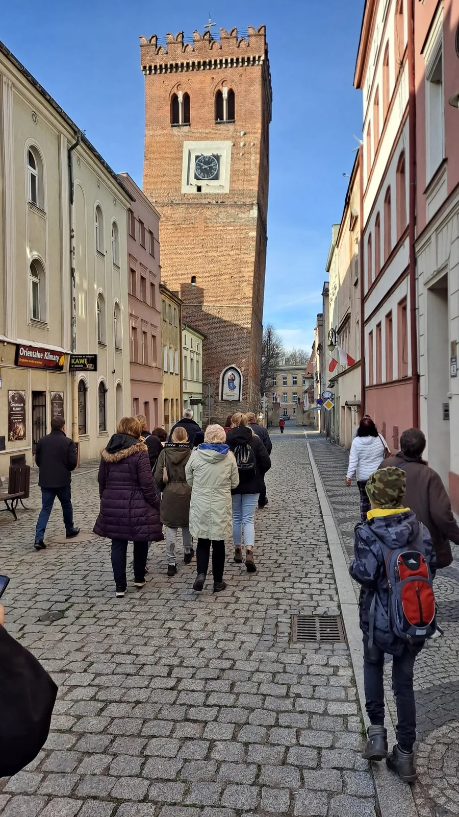 Grupa spaceruje brukowaną ulicą w stronę Krzywej Wieży w Ząbkowicach Śląskich.